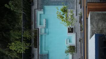 An aerial view of a modern outdoor swimming pool with geometric landscaping and seating areas.