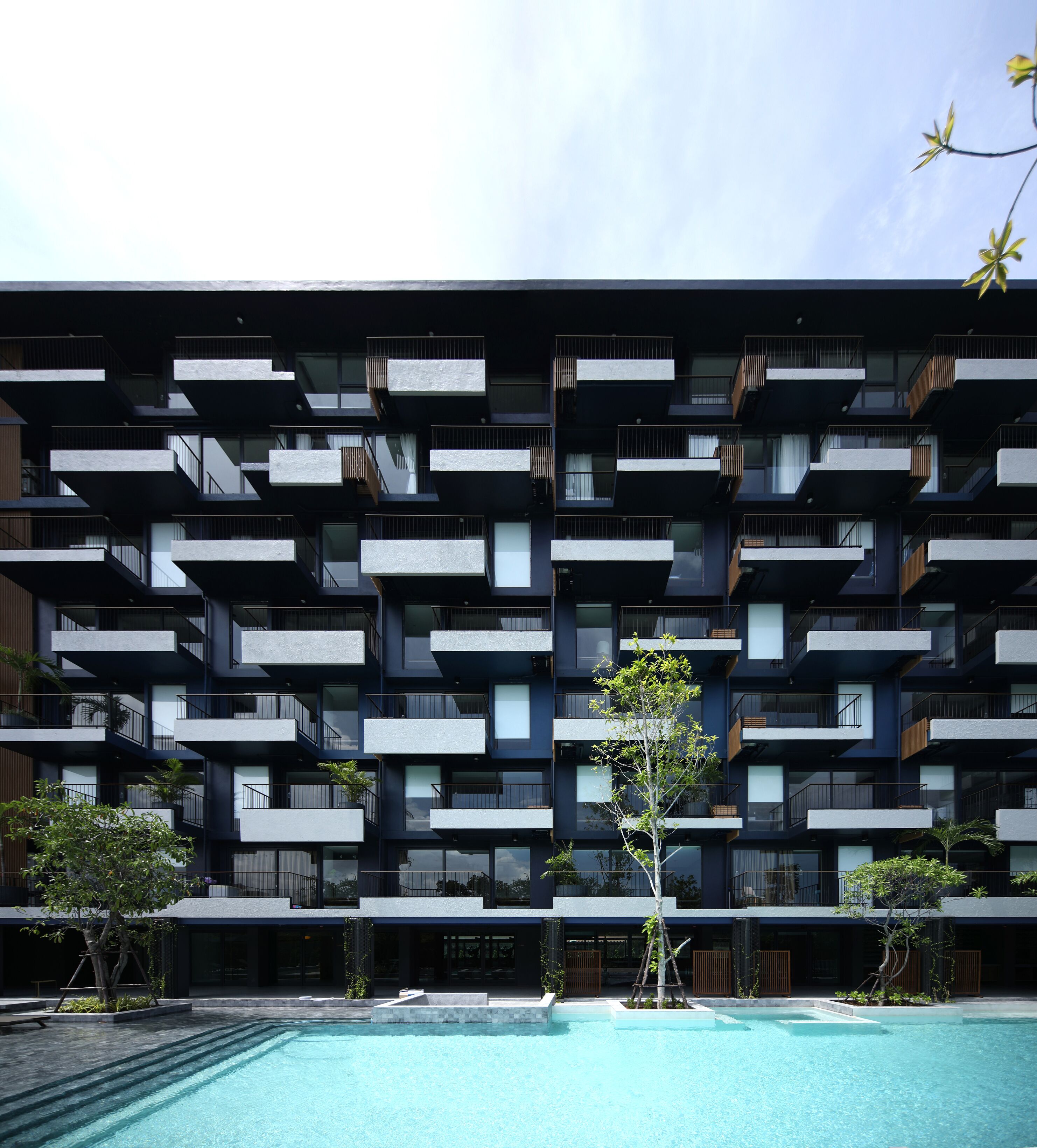 Un edifici modern d'àmbit elevat amb balcons i una piscina al davant.