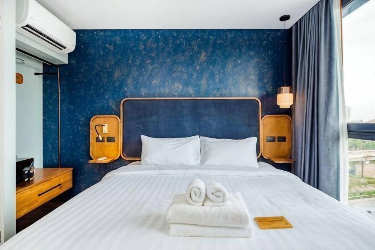 A hotel room with a large bed, a nightstand, a wall-mounted lamp, and a view through the window.