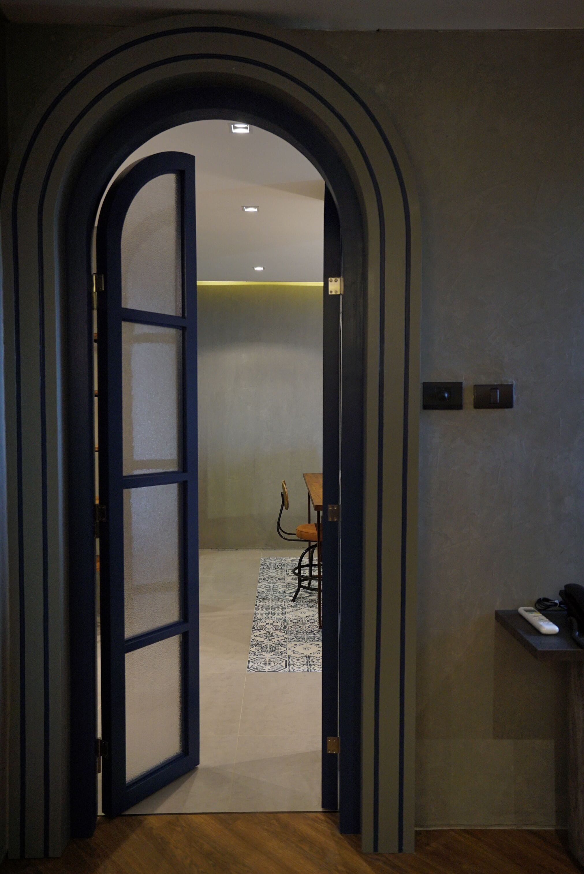 An interior view of a hallway with a wooden floor, a patterned rug, and a door leading to another room.