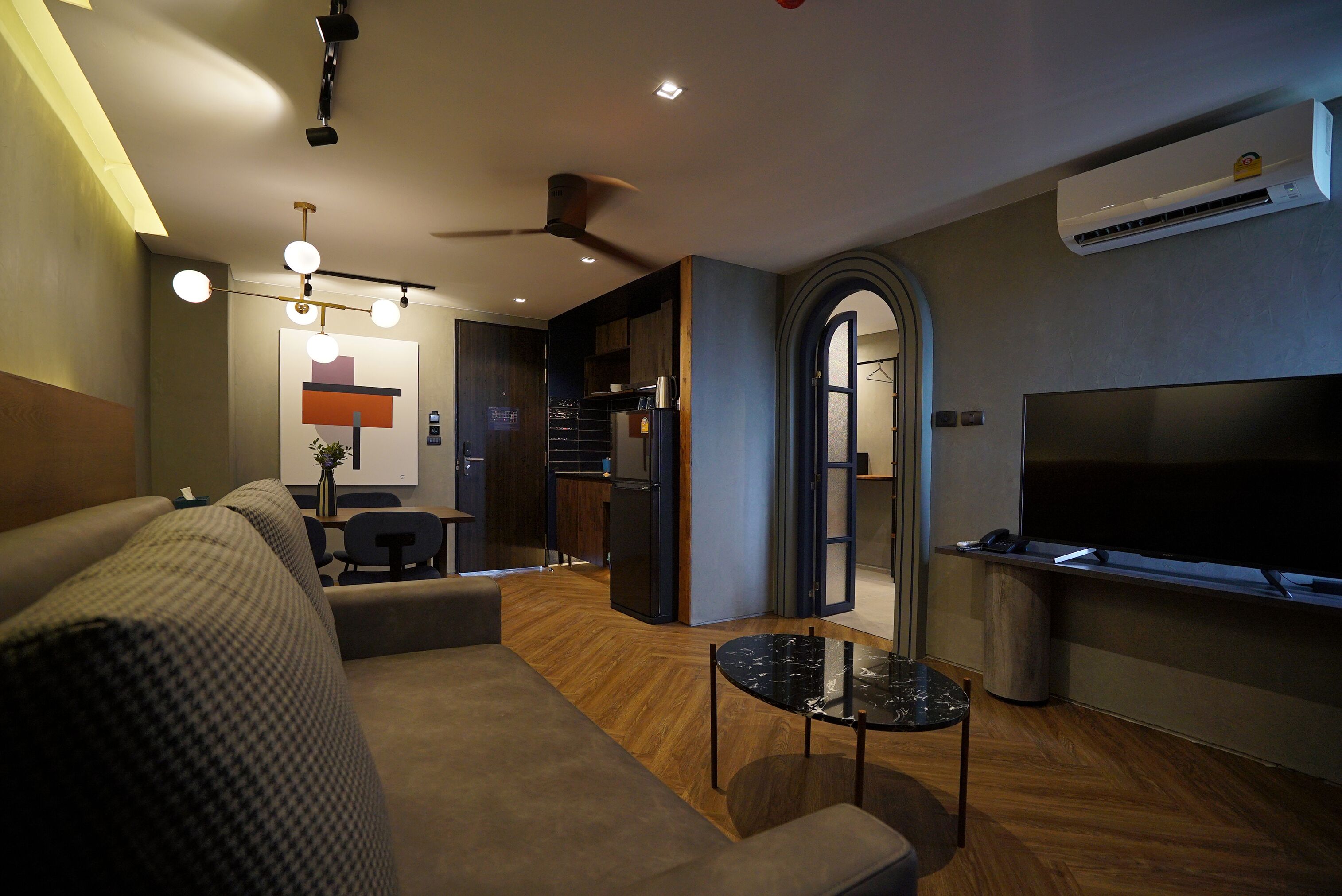 A modern living room with a sofa, a coffee table, a TV, and a kitchen area in the background.