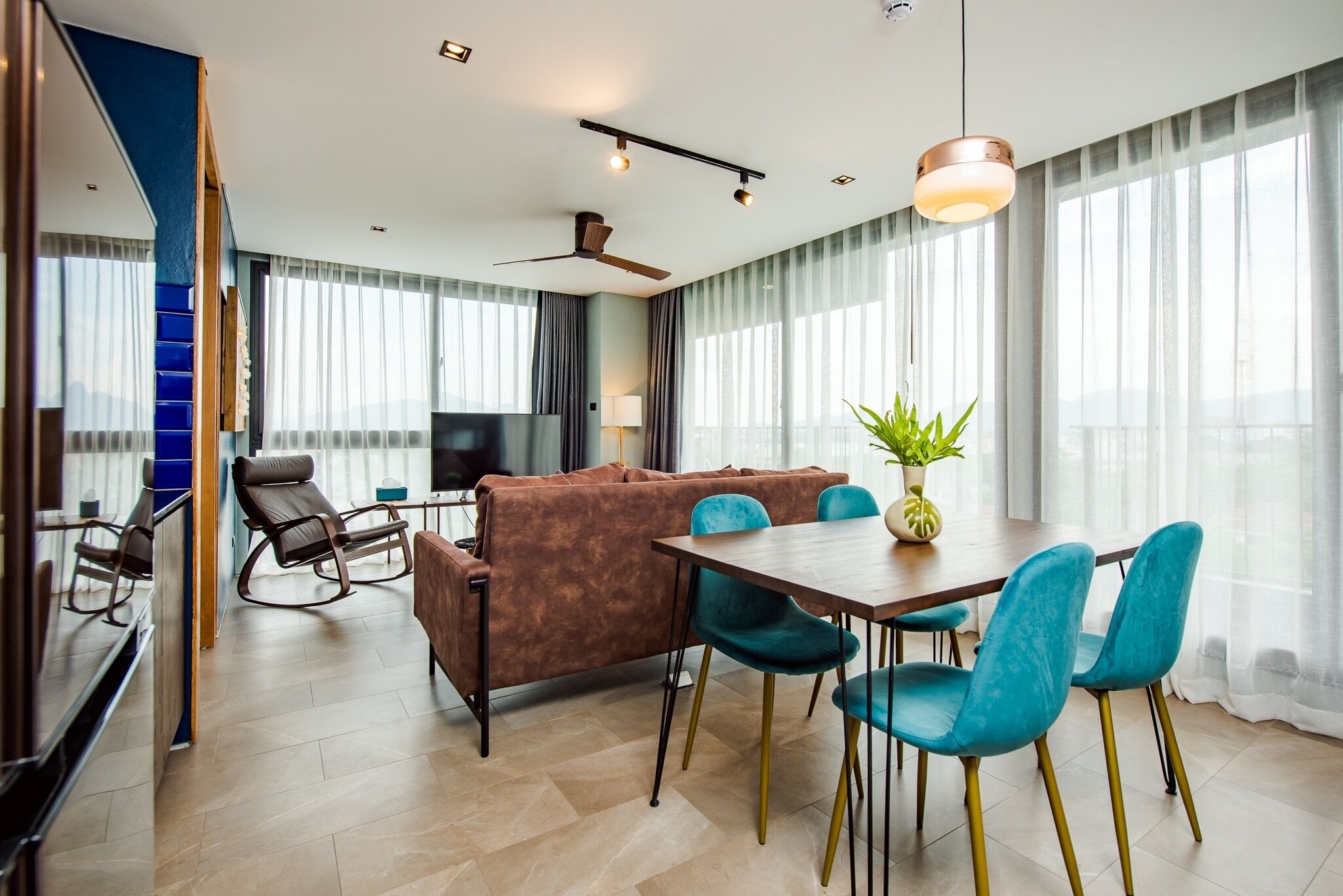 Una habitación de hotel moderna con sofá, mesa de comedor, sillas, televisor y ventilador de techo.