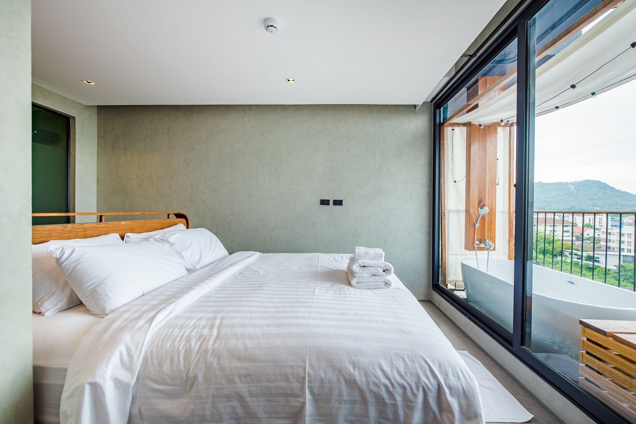 Une chambre d’hôtel moderne dotée d’un grand lit, offrant une vue sur le paysage urbain et comprenant un balcon avec une baignoire.