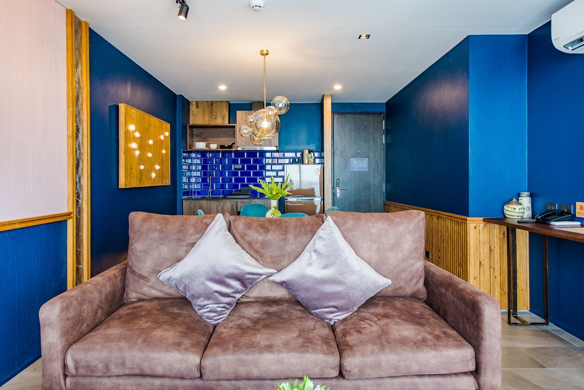 A modern living area with a brown sofa, a wooden accent wall, and a blue brick backsplash in the background.