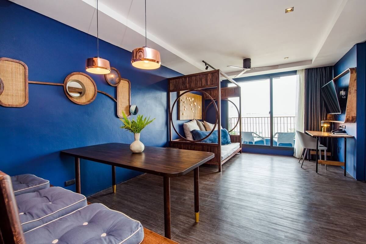 A modern living room with a blue wall, a wooden dining table, a sofa, and a hanging chair.