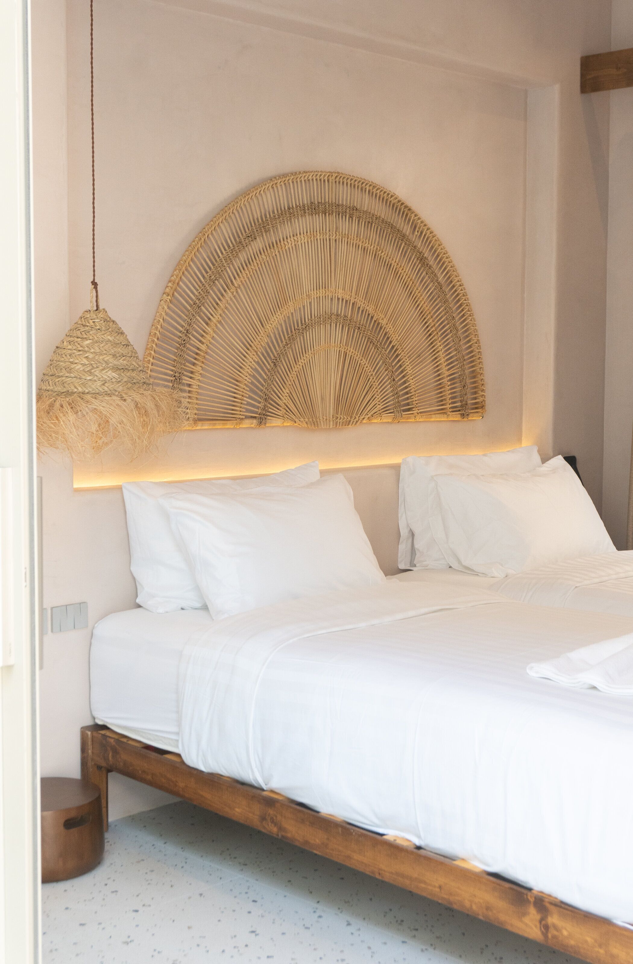 A bed with white linens, a wooden frame, and a woven headboard.