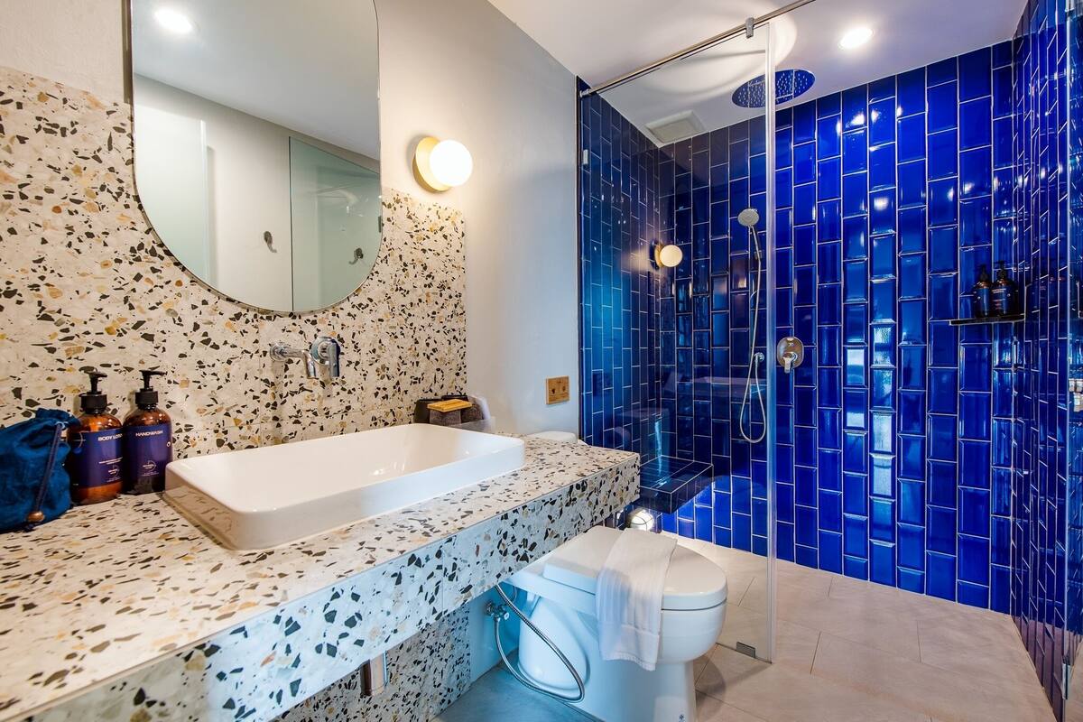 A bathroom with a white bathtub, a large mirror, and a shower with blue tiles.
