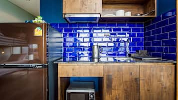 A compact kitchen with blue-tiled backsplash, wooden cabinets, a built-in microwave, and a stainless steel kettle.