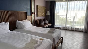 A hotel room with two beds, a wooden headboard, a small table, and a view of the outdoors through large windows.