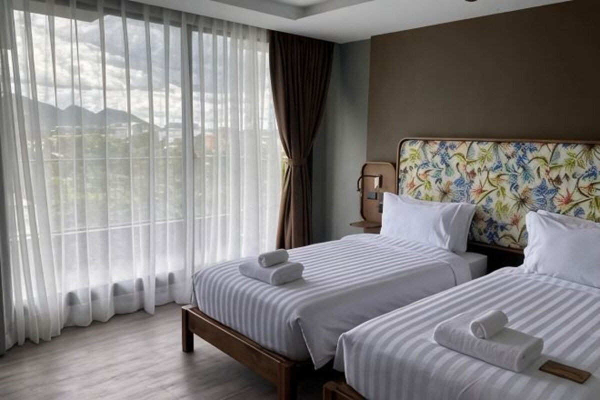Habitación de hotel con dos camas, un ventanal con cortinas translúcidas y vistas al exterior.