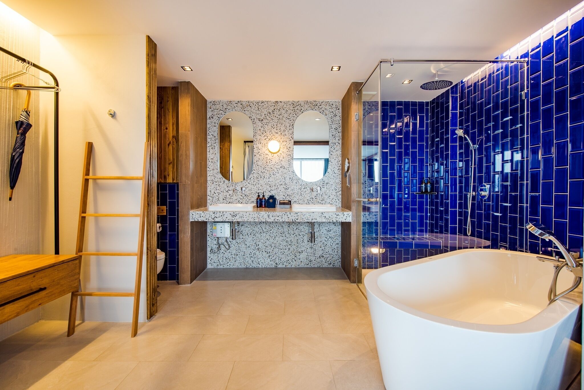 A modern bathroom with a freestanding bathtub, a wooden ladder, and a vanity with a mirror.