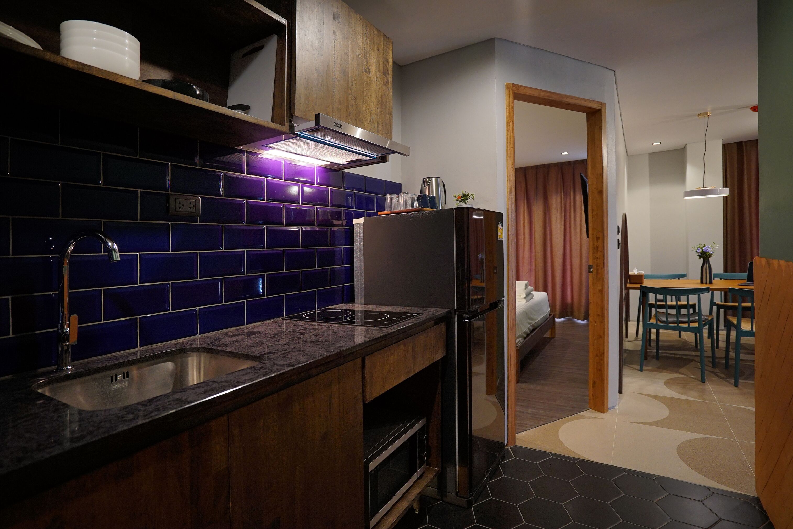 A modern kitchen with dark blue tiles, a stainless steel refrigerator, and a built-in oven.