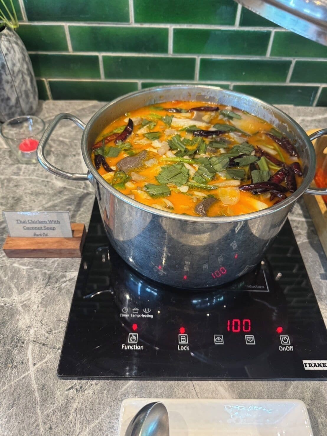 Una olla con sopa de pollo tailandesa y coco sobre una cocina por inducción digital ajustada a 100 grados Celsius.