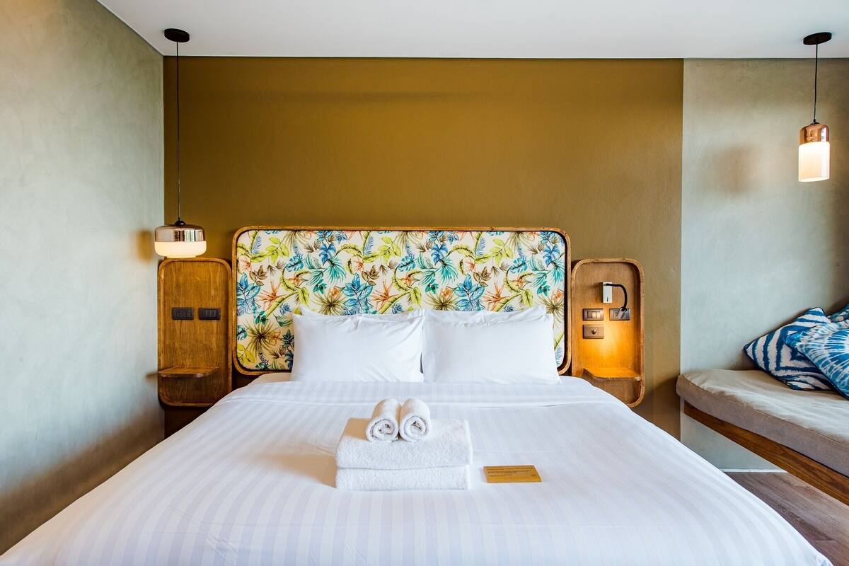 A hotel room with a bed, a nightstand, a bedside table, and a wall-mounted lamp.