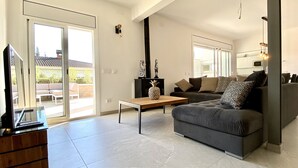Een moderne woonkamer met een grijze bank, een houten salontafel en een tv op een houten dressoir.