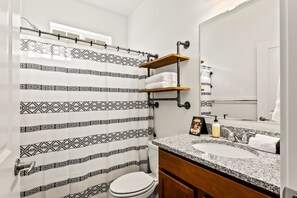 A bathroom with a patterned shower curtain, a sink with a granite countertop, and a wooden shelf above the sink. - Upscale Townhome | Near The Village & Boise Mall-67 (Boise)