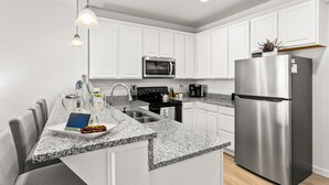 Une cuisine moderne avec des meubles blancs, un réfrigérateur en acier inoxydable, un four à micro-ondes et un plan de travail en granit.