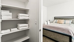 Une pièce bien rangée, avec un lit, une table de chevet et une étagère où sont pliées des serviettes.
