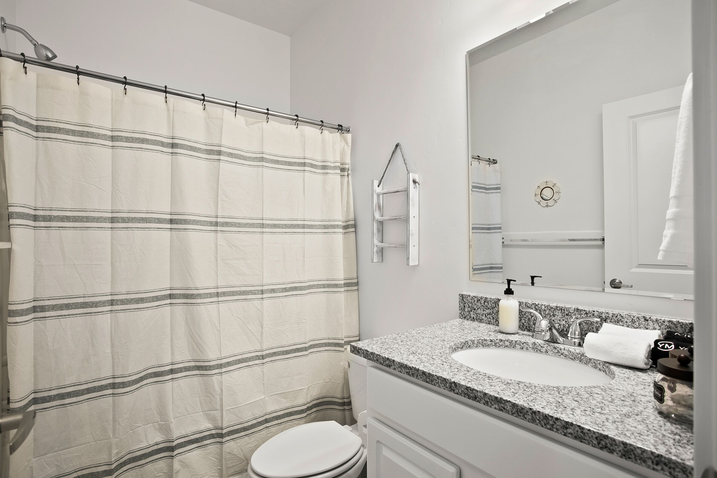 Ein Badezimmer mit gestreiftem Duschvorhang, Toilette, Waschtisch mit Granitplatte, Spiegel und Handtuchhalter.