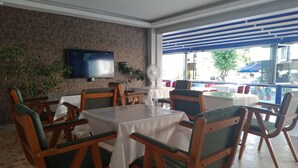 Ein Restaurant mit Tischen und Stühlen, einem an der Wand befestigten Fernseher und Blick ins Freie.
