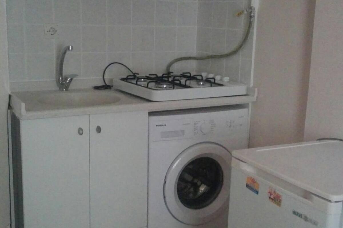 Uma cozinha compacta com armários brancos, fogão a gás, máquina de lavar e geladeira.