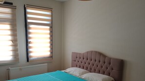 Ein Schlafzimmer mit Bett, Nachttisch, Heizkörper und einem Fenster mit Jalousien.