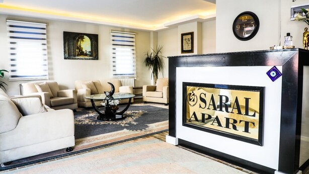 Ein modernes Wohnzimmer mit einer Couch, Sesseln, einem Couchtisch und einem Empfangstresen mit der Aufschrift "SARAL APART".