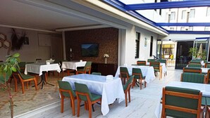 Ein Restaurant mit Außenbestuhlung, Tische mit weißen Tischdecken und grüne Stühle.