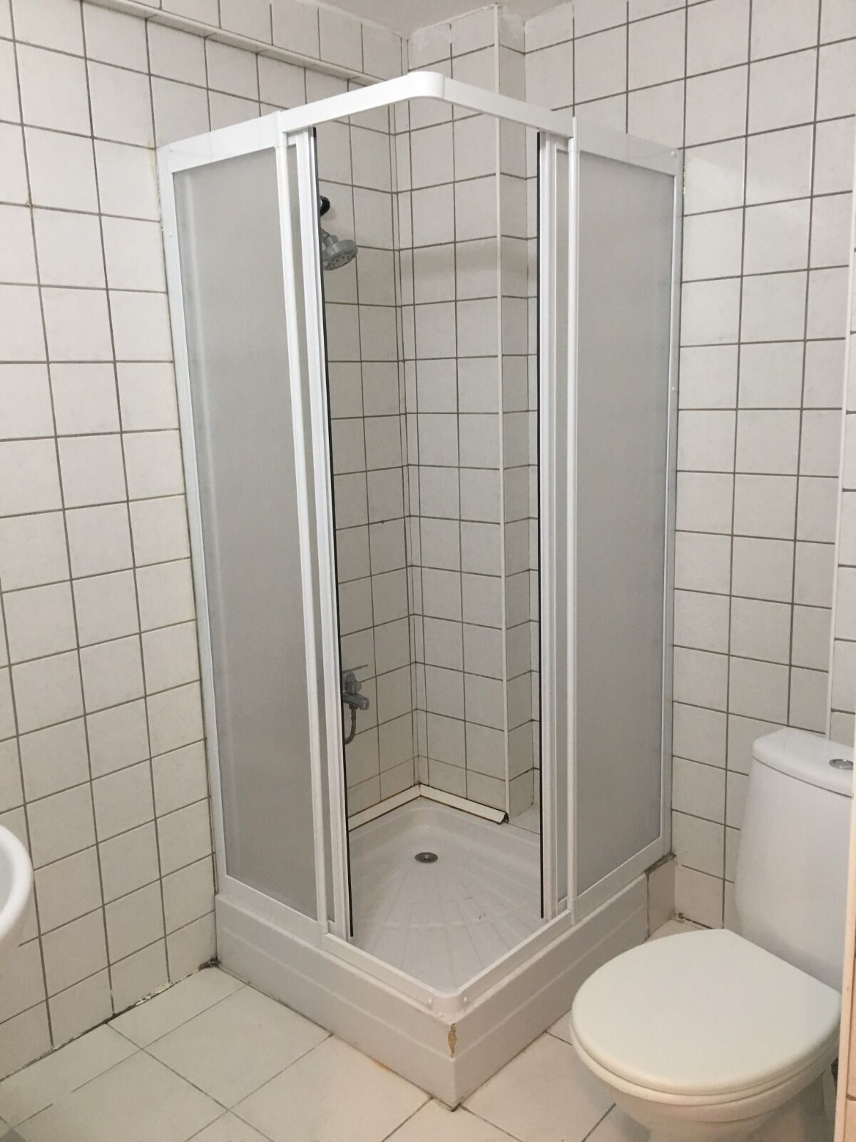 A small, tiled bathroom with a glass-enclosed shower, a toilet, and a sink.