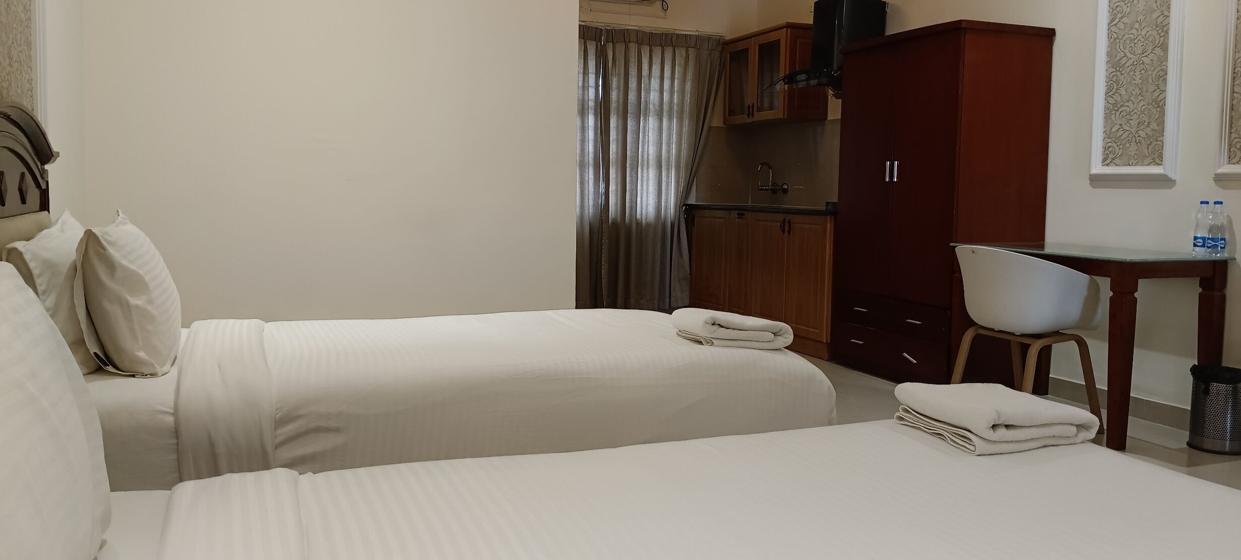 A hotel room with two beds, a desk, a chair, a wardrobe, and a curtain.