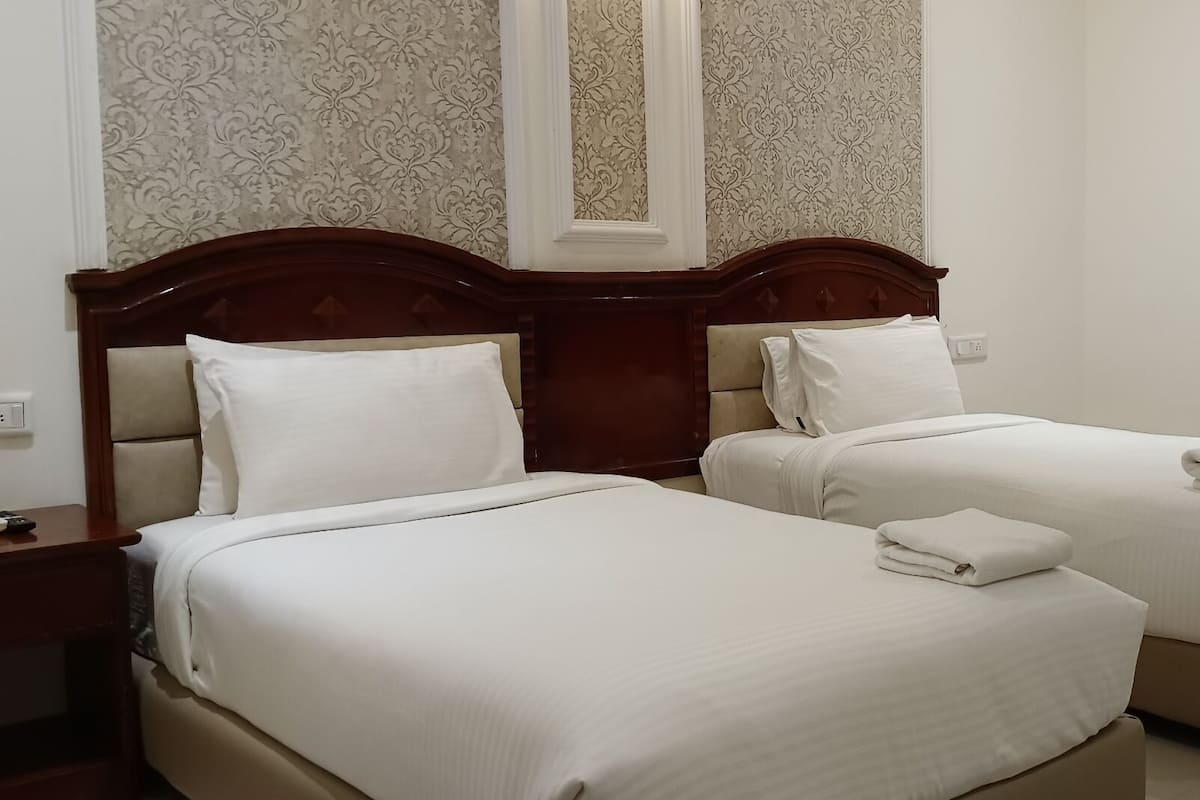 Habitación de hotel con dos camas, cada una con cabecero de madera, ropa blanca y una toalla doblada sobre las camas.