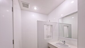 Ein modernes Badezimmer mit weißen Fliesen, einer Duschkabine, einem Waschbecken mit Spiegel und einer Toilette.