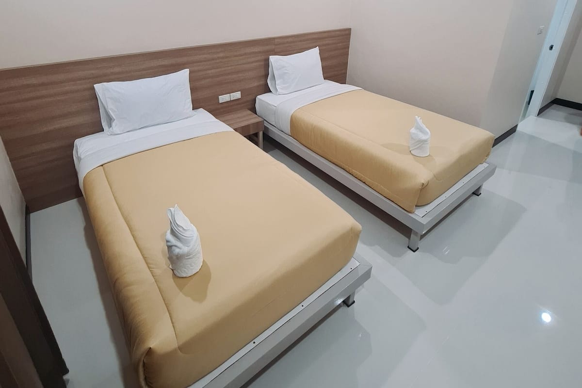 Habitación de hotel con dos camas, cada una con cabecero de madera, ropa de cama blanca y una toalla sobre las camas.