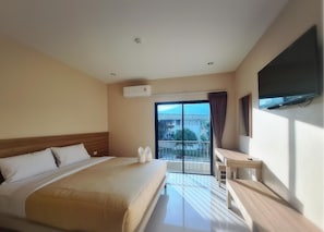 A hotel room with a large bed, a desk, a flat-screen TV, and a balcony with a view of buildings. - Grand Maihom Hotel (Chiang Mai)