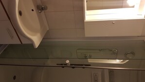 Een badkamer met een douchecabine van glas, een wastafel en een spiegel.