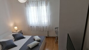Een slaapkamer met een bed, nachtkastje, lamp, raam met gordijnen en een stoel.