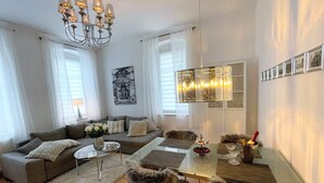 Una sala de estar moderna con una mesa de comedor de vidrio, un sofá, una lámpara de araña y una galería de cuadros en la pared.