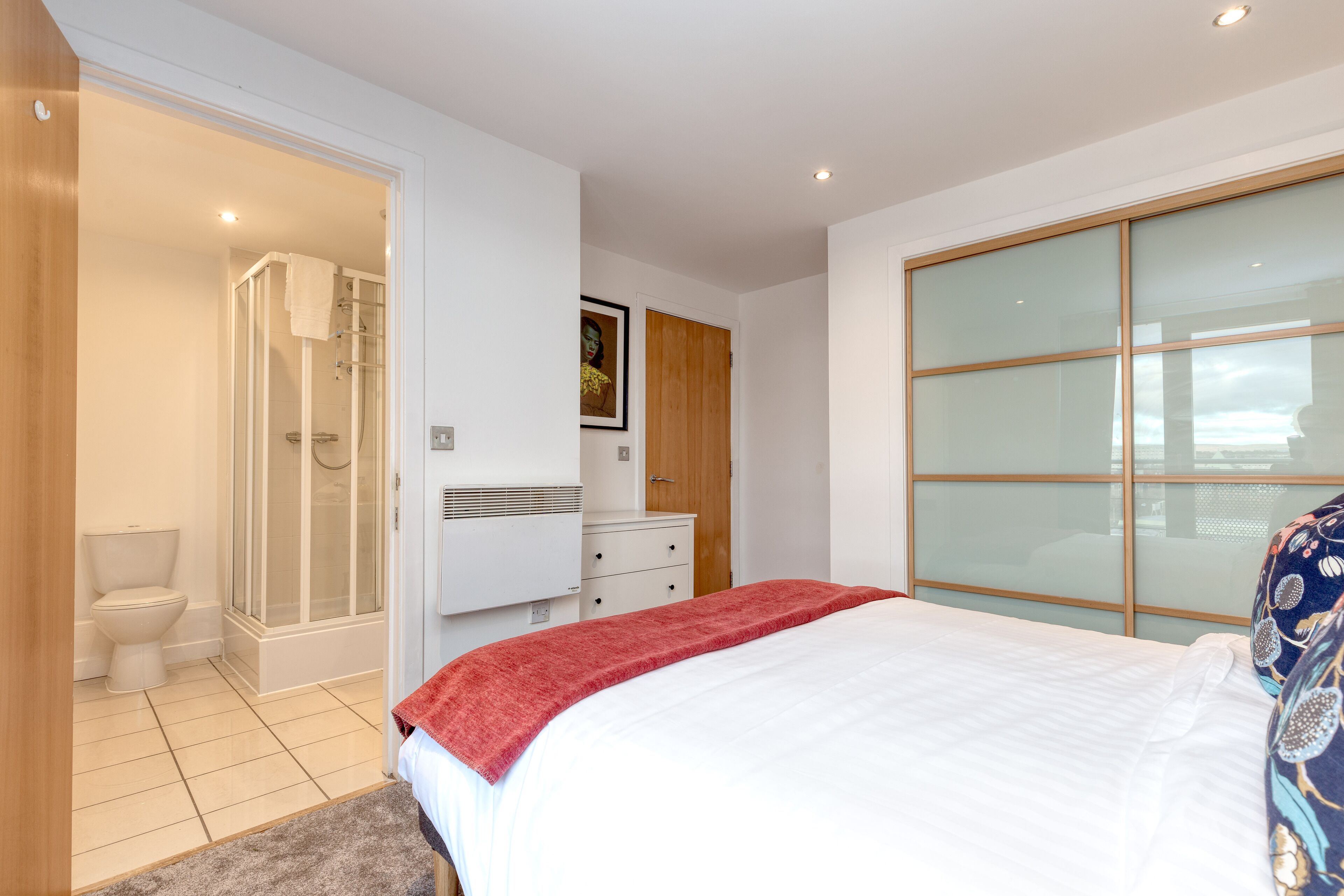 A modern bedroom with a bed, a shower, a toilet, and a wardrobe.