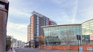 A modern urban street with high-rise buildings, including a glass-fronted structure and a building under construction. - Riverview Apartments (Glasgow)
