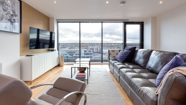 A modern living room with a leather sofa, a coffee table, and a TV on a white console. - Riverview Apartments (Glasgow)