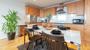 A modern kitchen with wooden cabinets, a central island with seating, and a potted plant. - Riverview Apartments (Glasgow)