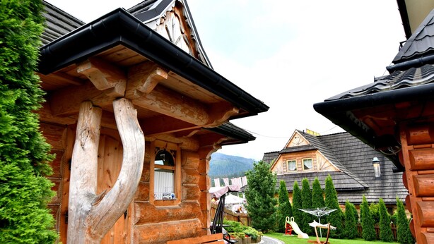A wooden building with a curved roof and a bench outside. - Willa Dziubas (Poronin)