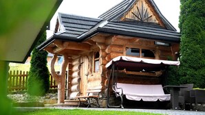A wooden log cabin with a sloped roof and a covered outdoor seating area. - Willa Dziubas (Poronin)