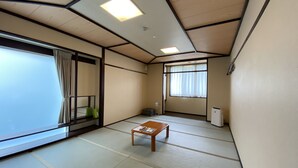 Een traditionele Japanse kamer met tatami vloerbedekking, een lage houten tafel, schuifdeuren en een groot raam met gordijnen.