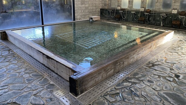Een wellnessruimte met een bubbelbad, stenen vloer en uitzicht op een tuin via een glazen deur.