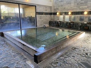 A spa area with a hot tub, stone flooring, and a view of a garden through a glass door. - Green Hills New Minami (Yamanakako)