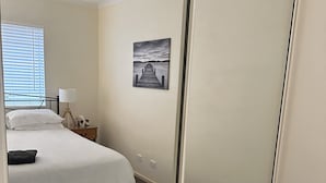 A bedroom with a bed, bedside table, lamp, and a painting on the wall. - Cosy Apartment close to everything (North Adelaide)
