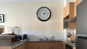 A modern kitchen with wooden cabinets, a stainless steel sink, and a microwave. - Cosy Apartment close to everything (North Adelaide)