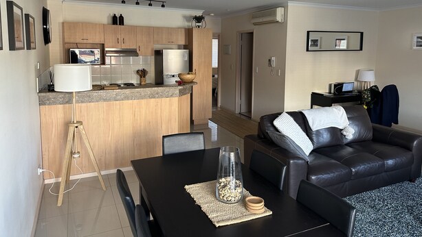 A modern living room with a black leather sofa, a dining table with chairs, and a kitchen area with a refrigerator and microwave. - Cosy Apartment close to everything (North Adelaide)