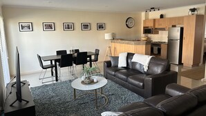 A modern living room with a sofa, coffee table, and dining area. There is a kitchen with a microwave, stove, and refrigerator. - Cosy Apartment close to everything (North Adelaide)